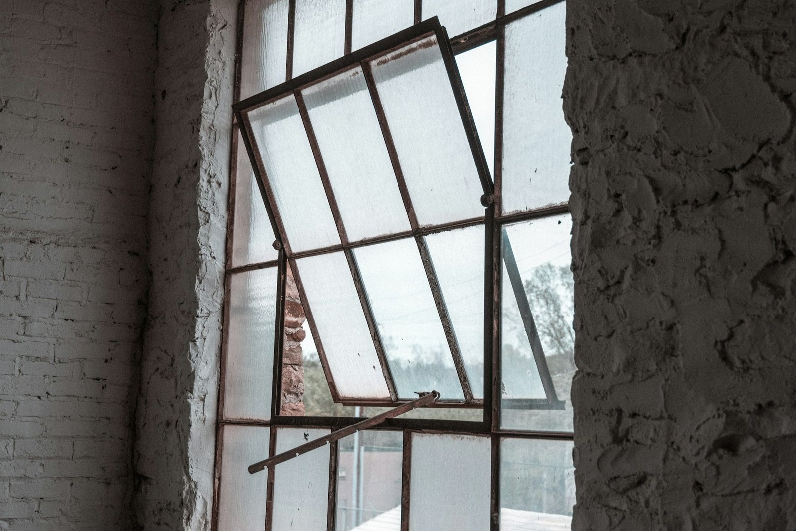 Hand prüft ein Metallscharnier an einem geöffneten Fenster